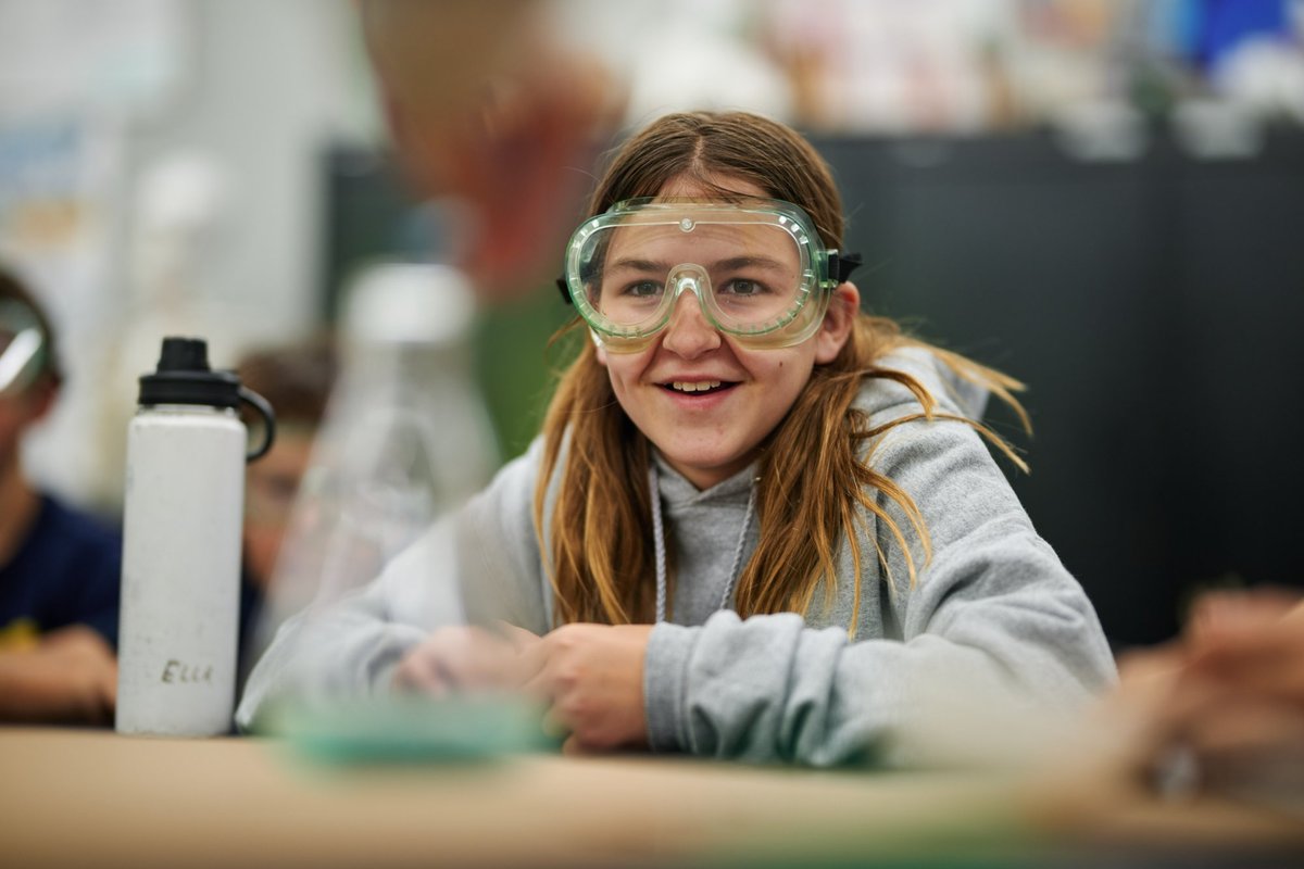 Middle school student in safety goggles smiling during a science lab